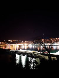 Illuminated bridge over river in city against clear sky at night