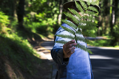 A man in a forest is covered by a fern leaf. man with a vest and denim shirt
