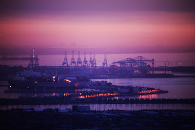 Illuminated commercial dock by river against sky at sunset