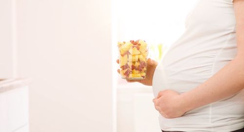 Midsection of pregnant woman holding glass with fruits at home