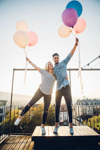 Young man and woman holding balloons against sky