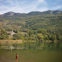 Boy standing in lake by mountains against sky