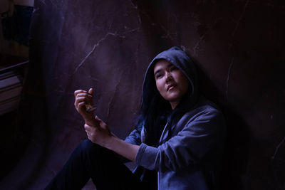 Woman wearing hooded shirt sitting against wall