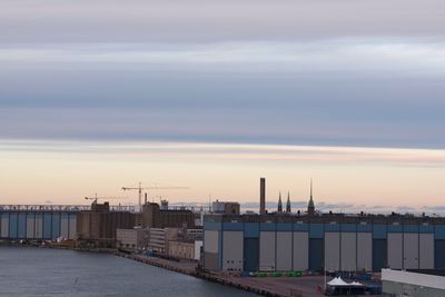 Factory by sea against sky during sunset