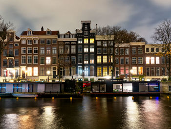 Buildings by river against sky at sunset