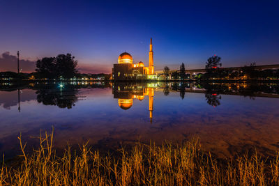 Illuminated built structure by lake against sky at night