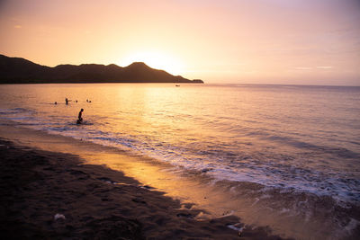 Silhouette people in sea against sky during sunset