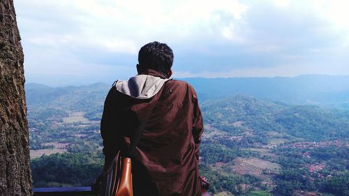 Rear view of man standing on mountain against sky