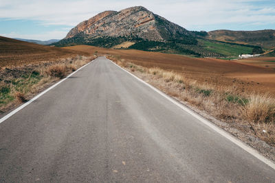 Empty road by mountains against sky