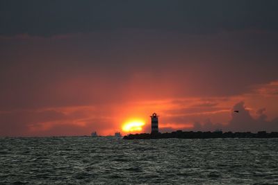 Silhouette lighthouse by sea against sky during sunset