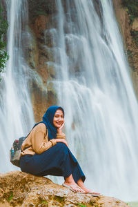 Portrait of man sitting on rock against waterfall