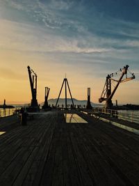 Cranes at pier against sky during sunset