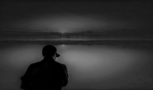 Rear view of silhouette man standing by lake against sky