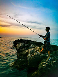 Side view of man fishing in sea against sky