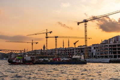 Cranes at construction site against sky during sunset