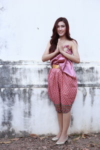 Portrait of a smiling young woman standing against wall