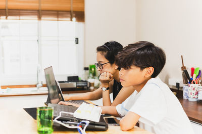 Side view of young mother and son working on laptop at home