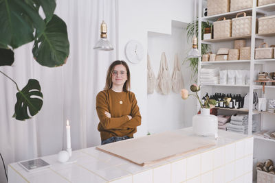 Portrait of young female entrepreneur standing arms crossed at desk in studio