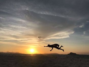 Silhouette man jumping over sea against sky during sunset