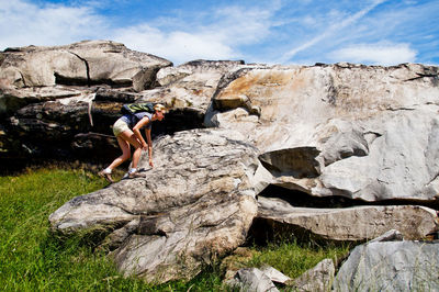 Female hiker climbing on rock formation against sky during sunny day