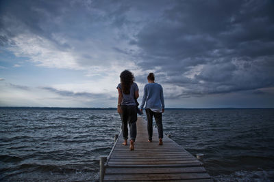 Rear view of female friends walking on jetty against sky