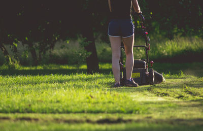 Low section of woman mowing lawn in yard