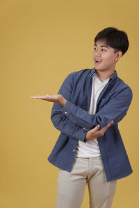 Portrait of teenage boy standing against yellow background