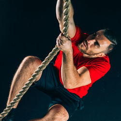 High angle view of male athlete climbing on rope in gym