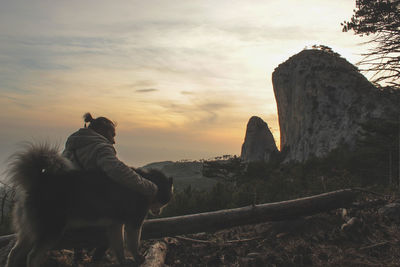 Man with dog sitting on mountain against sky