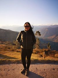 Portrait of woman wearing sunglasses standing on mountain against sky