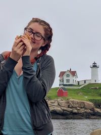 Young woman eating food standing against house outdoors