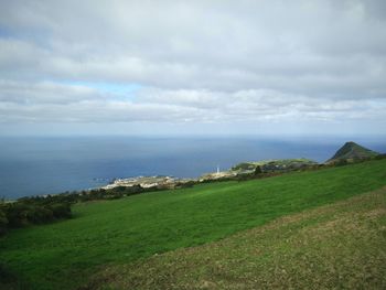 Scenic view of field by sea against sky