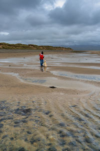 Woman with dog standing at beach against cloudy sky