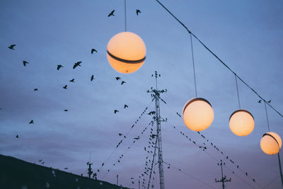 Low angle view of illuminated lights against bird flying in sky at sunset