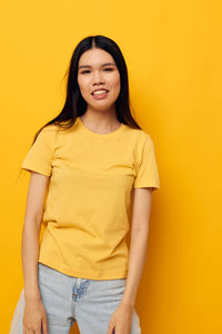 Portrait of young woman standing against yellow background