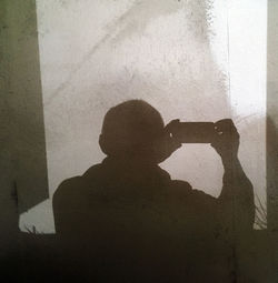 Silhouette man photographing against wall