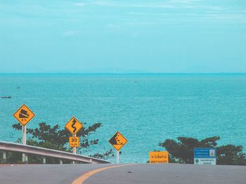 Road sign by sea against blue sky