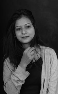 Portrait of beautiful young woman standing against black background