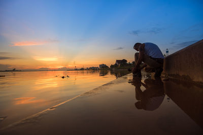 Man standing on shore against sky during sunset