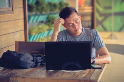 Mid adult man checking phone while using laptop on table at home