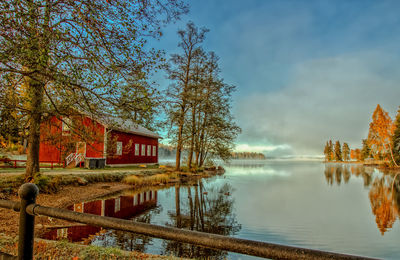 Scenic view of lake by houses and trees against sky