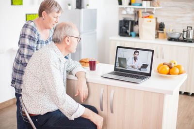 Rear view of couple talking with doctor on video call