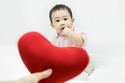 Cute baby boy holding heart shape against white background