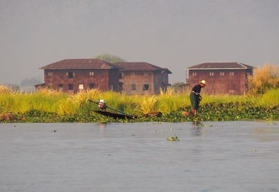 Man on house by lake against sky