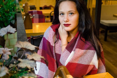 Portrait of young woman wrapped in blanket sitting at restaurant