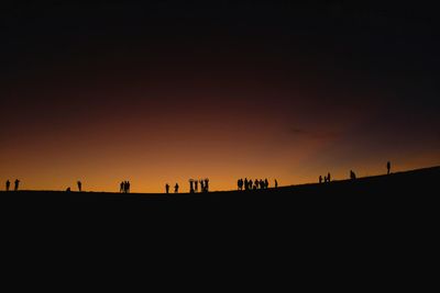 Silhouette people on field against clear sky during sunset