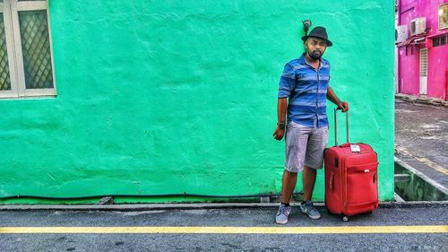 Portrait of male tourist standing by green wall in city