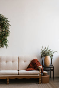 Stylish christmas tree in a pot stands near a white sofa with pillows in the living room