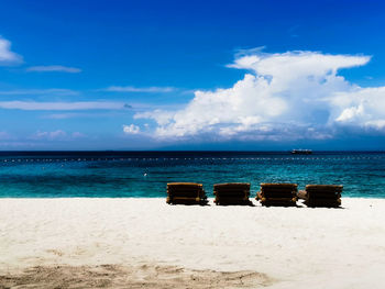 Deck chairs on beach against sky
