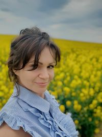 Portrait of smiling woman with yellow flower on field